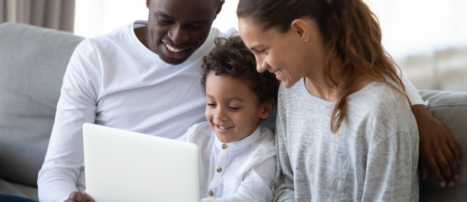 Glad familj av som sitter tillsammans pa en bekvam soffa i vardagsrummet och haller i barbar dator Glad familj av som sitter tillsammans pa en bekvam soffa i vardagsrummet och haller i barbar dator