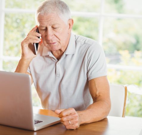 Koncentrerad aldre man som ar hemma sitter vid sin barbara dator och pratar i telefon Koncentrerad aldre man som ar hemma sitter vid sin barbara dator och pratar i telefon