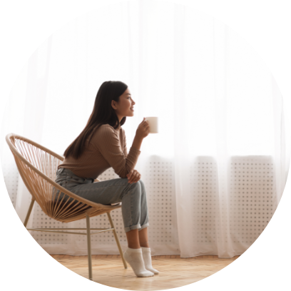 Ung flickas i stol som tycker om kaffe framfor fonstret sidovy@2x